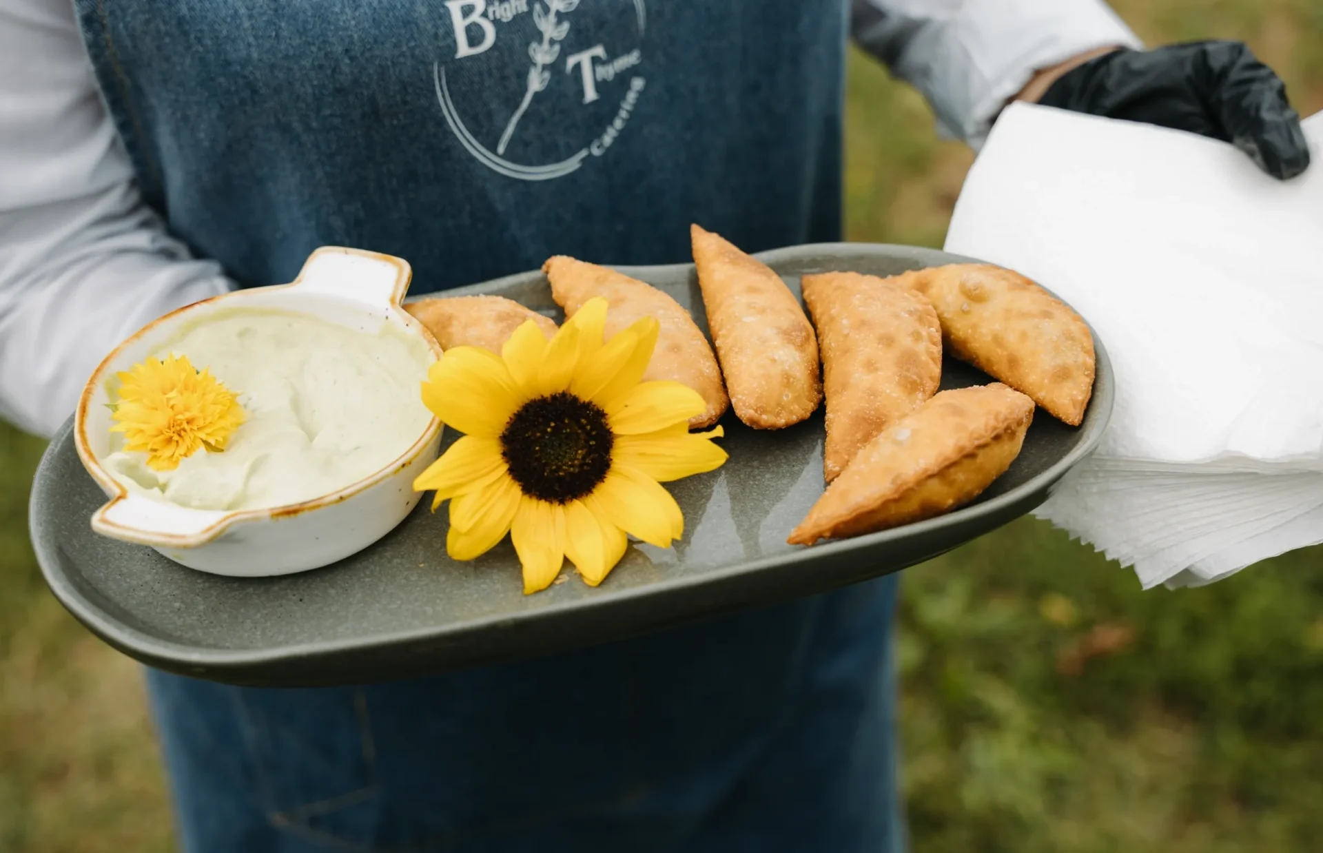 Tray with golden samosas, white sauce, and a sunflower.