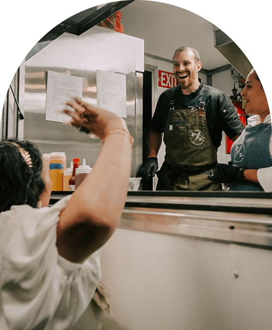 Two men cheerfully interacting through a food truck window.